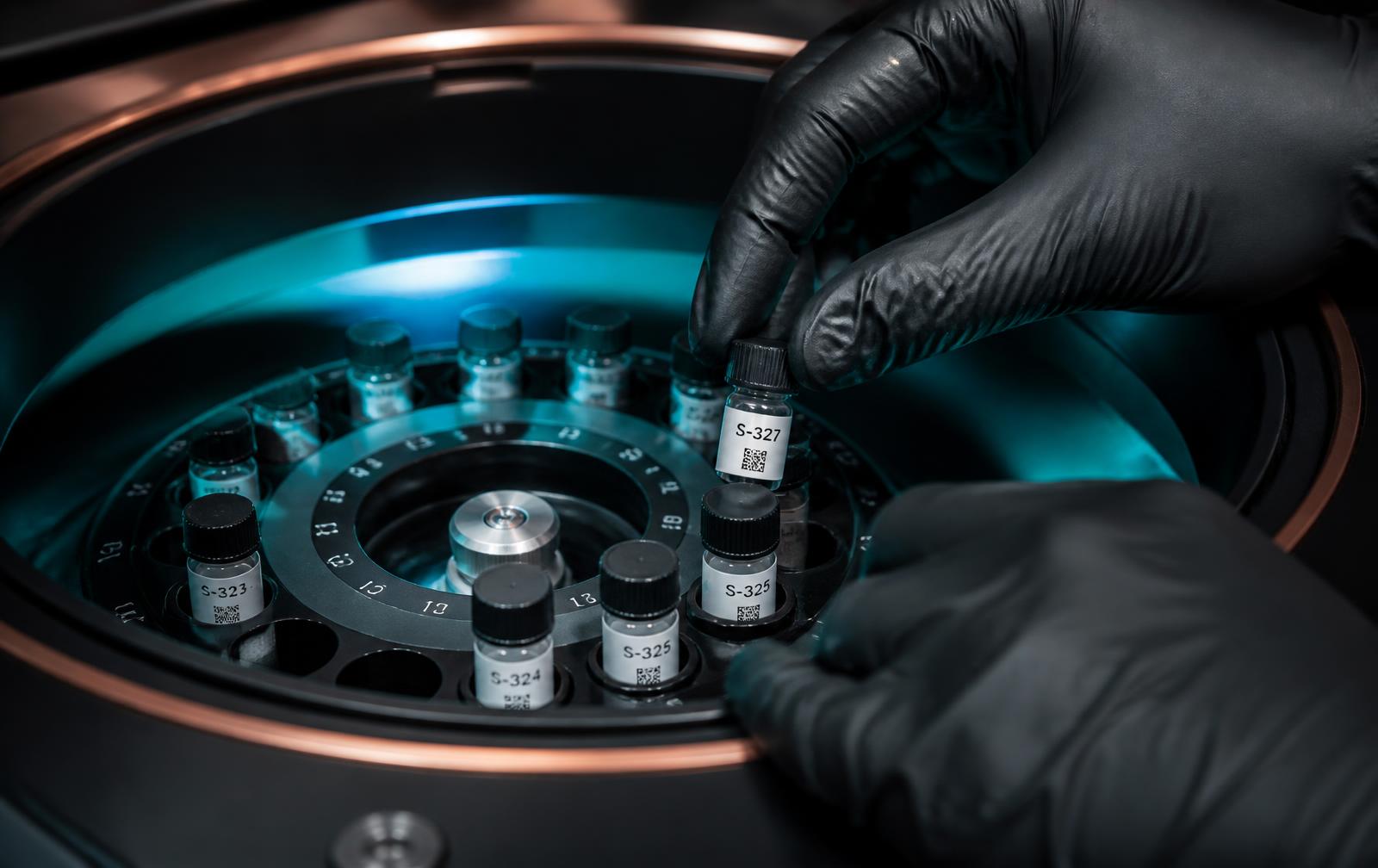 Gloved hands loading labeled clinical sample vials into a centrifuge